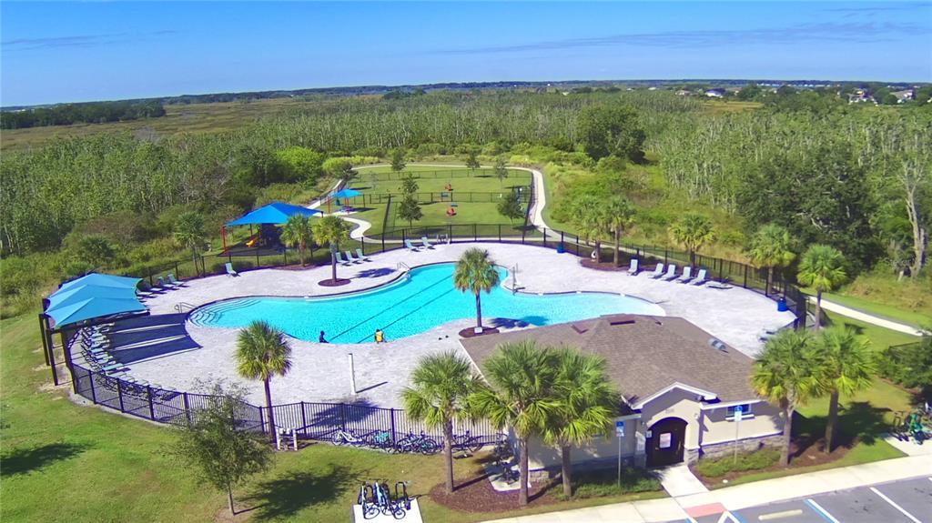 An aerial view of a swimming pool, clubhouse, and fenced dog park surrounded by trees — 5148 HELM STREET, HAINES CITY, FL