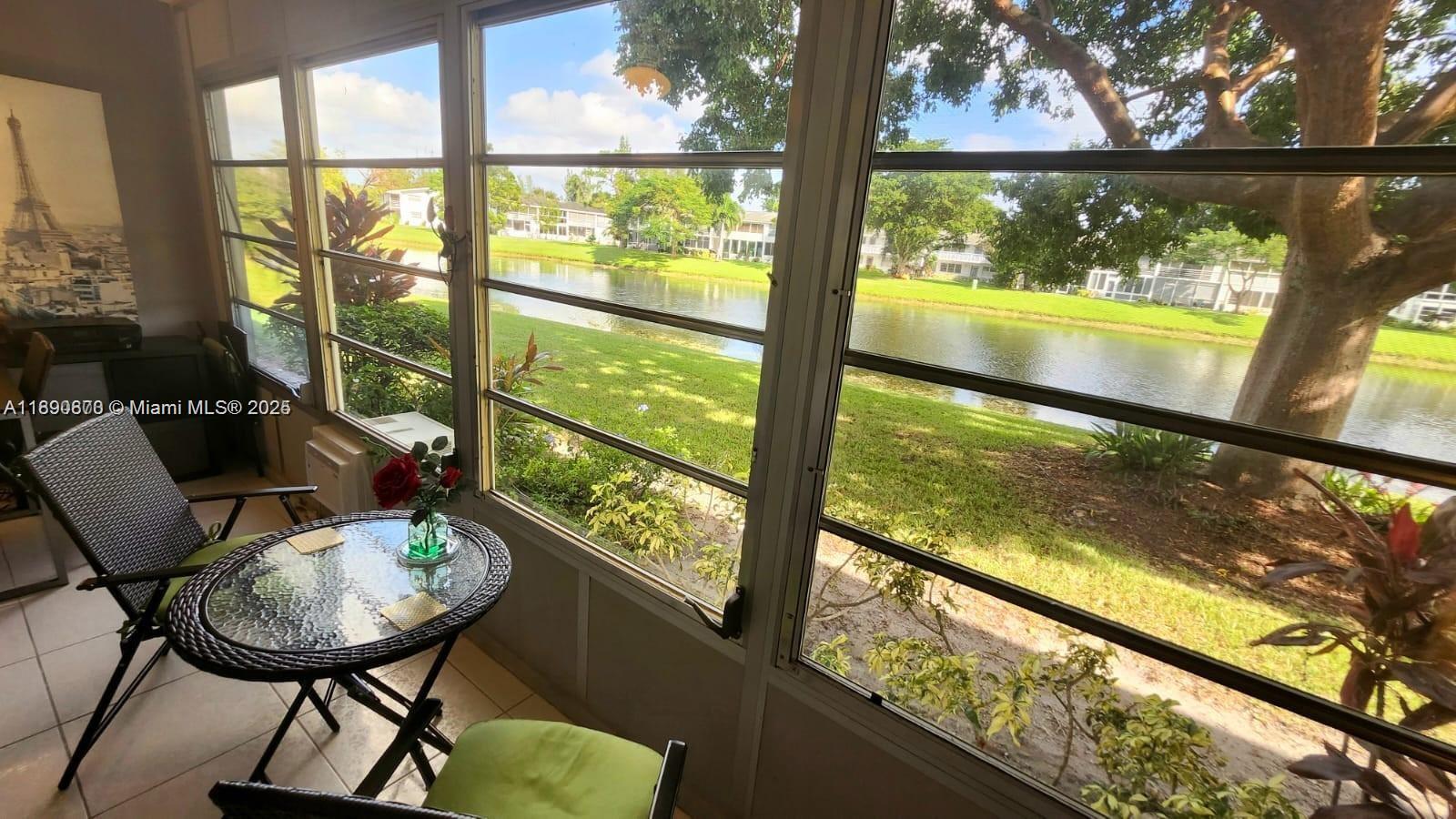 A sunroom features a small bistro table and chairs overlooking a lake and trees — 182 Ellesmere D # 182, Deerfield Beach FL 33442, DEERFIELD BEACH, FL