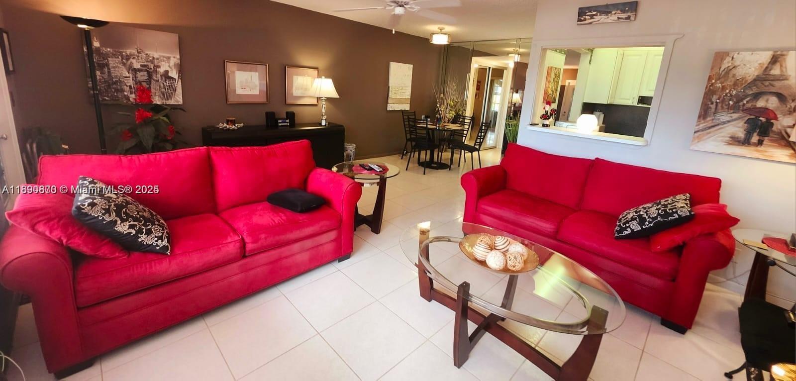 A living room features two red sofas, a glass coffee table, and tile flooring — 182 Ellesmere D # 182, Deerfield Beach FL 33442, DEERFIELD BEACH, FL