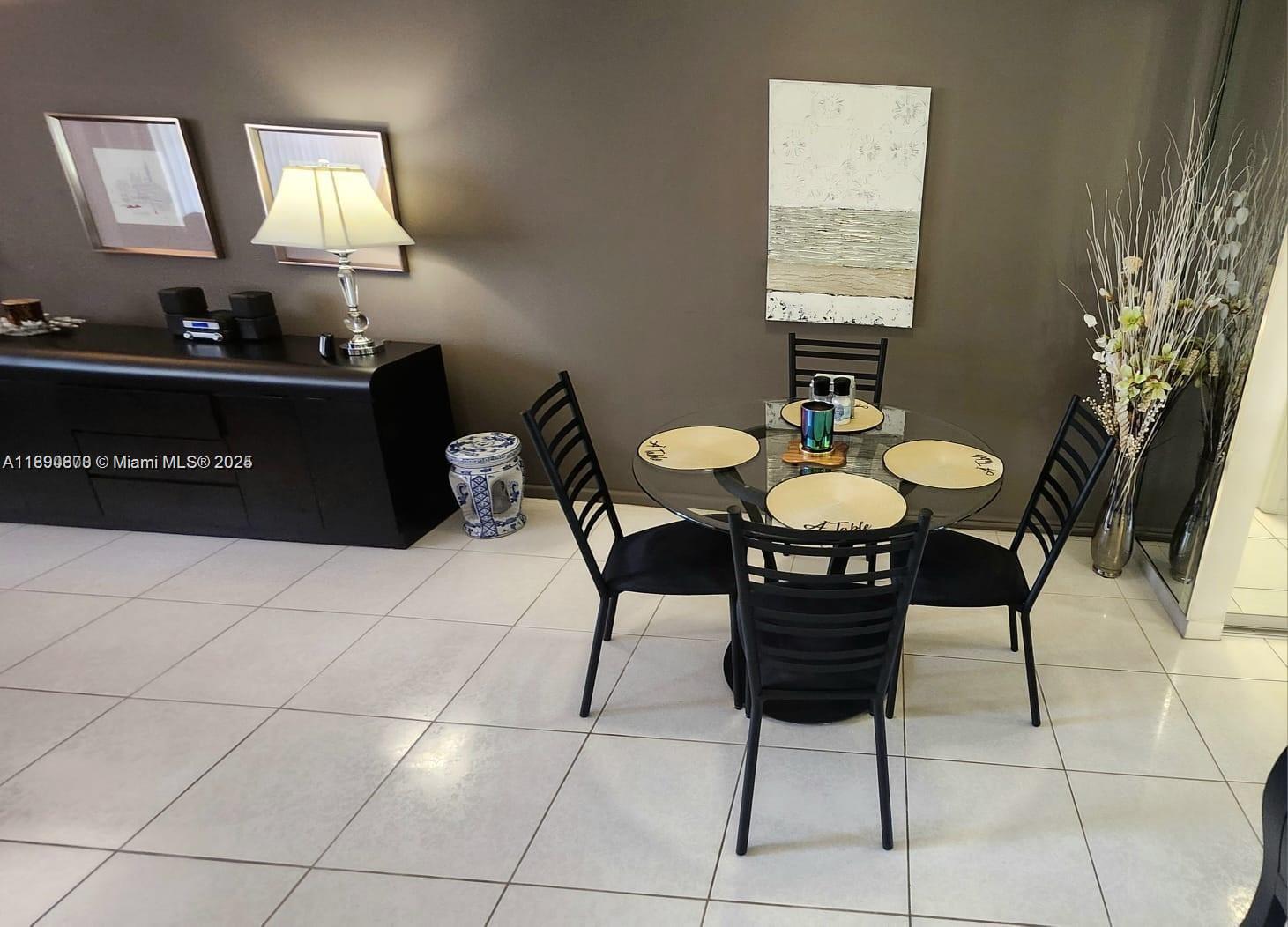 A dining area features a glass-topped table with four black chairs on tiled flooring — 182 Ellesmere D # 182, Deerfield Beach FL 33442, DEERFIELD BEACH, FL
