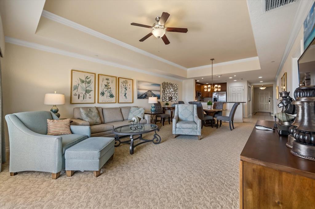 A living room with a tray ceiling, carpeted floors, and an open-concept kitchen in back — 1114 SUNSET VIEW CIRCLE UNIT 402, REUNION, FL