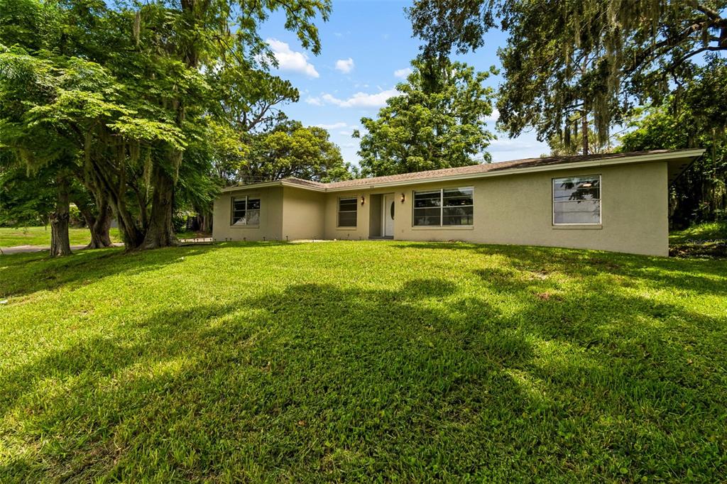 A single-story house with a beige stucco exterior sits on a grassy lawn under trees — 400 E SILVER STAR ROAD, OCOEE, FL