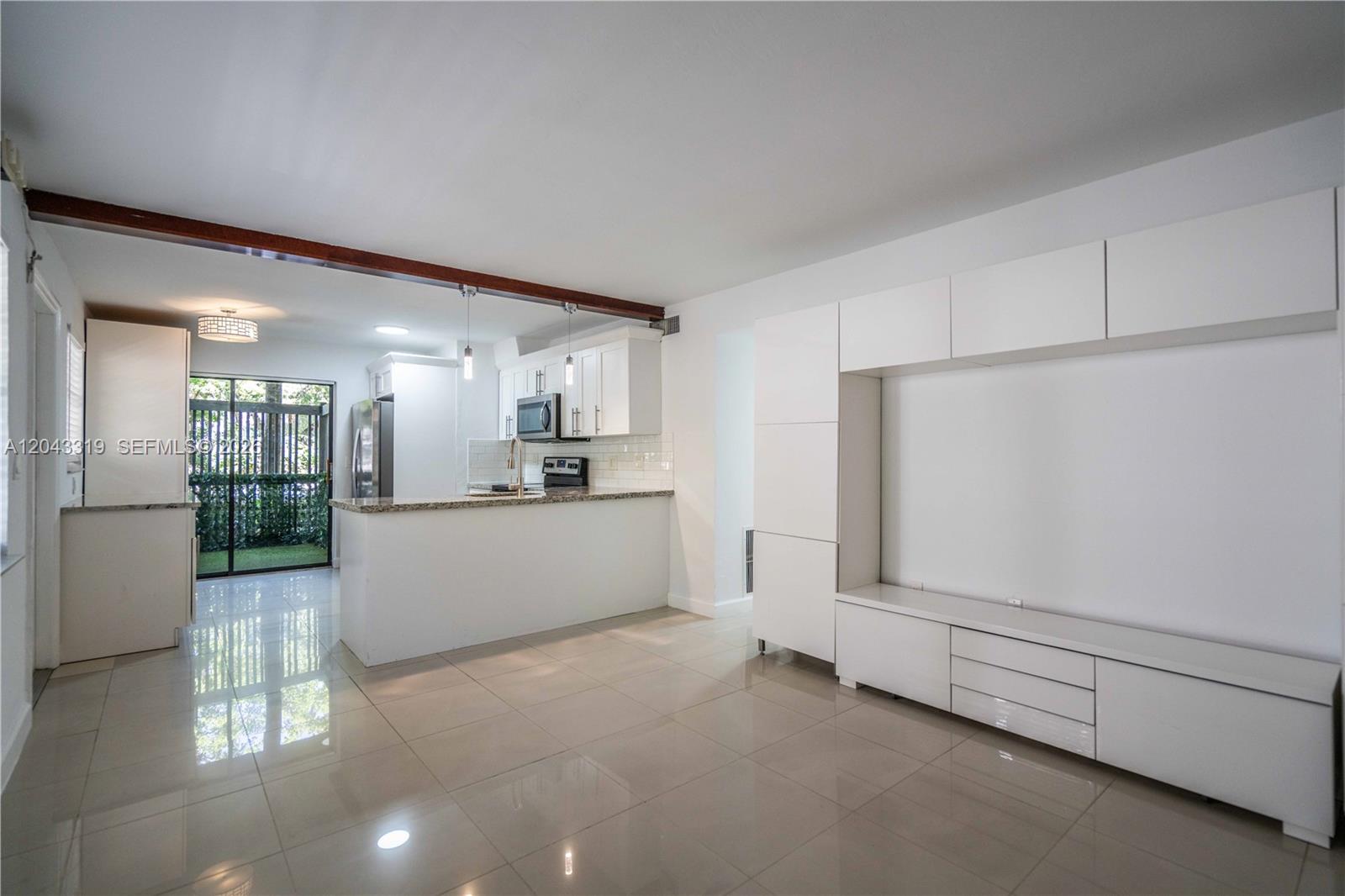 A bright living room with white cabinetry and tile flooring opens to a kitchen area — 3265 Virginia St # 1, Miami FL 33133, MIAMI, FL