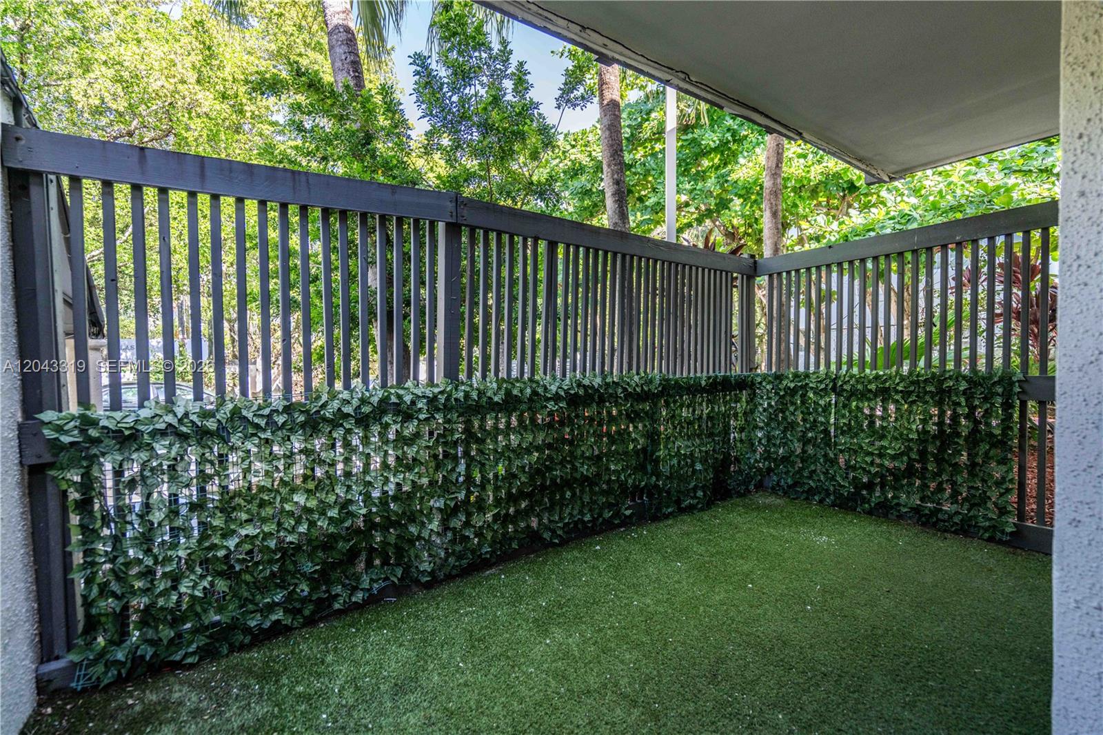 A small outdoor patio features artificial turf flooring and a wooden privacy fence with greenery — 3265 Virginia St # 1, Miami FL 33133, MIAMI, FL