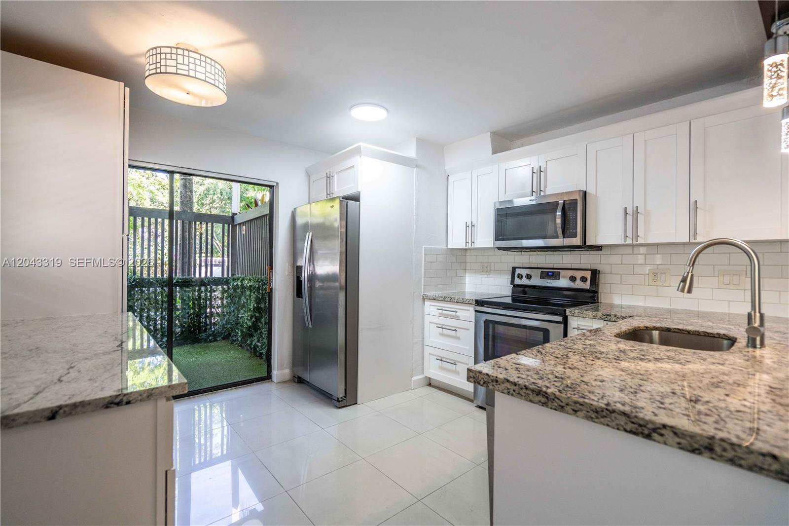 A modern kitchen features white cabinets, granite countertops, stainless steel appliances, and a sliding door — 3265 Virginia St # 1, Miami FL 33133, MIAMI, FL