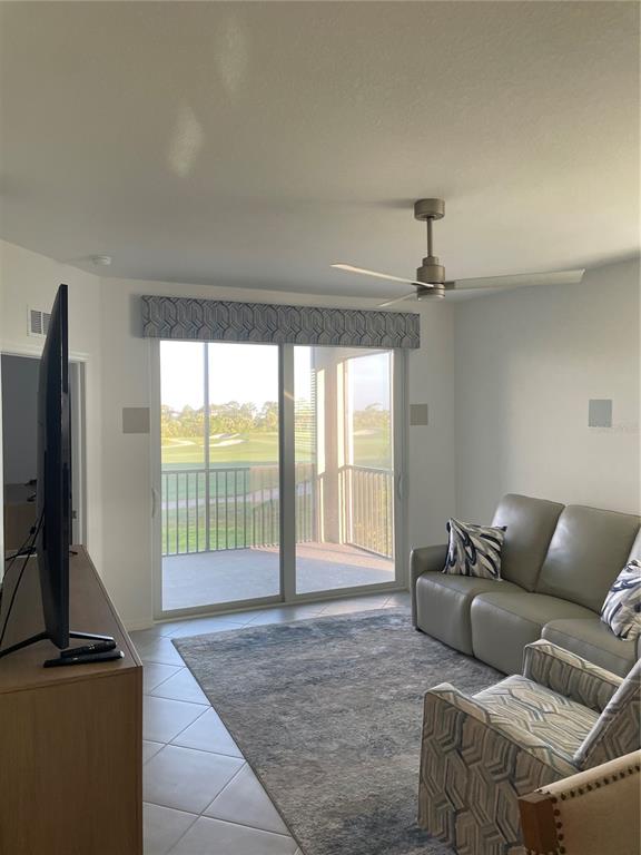 A living room features a gray sofa, patterned armchair, ceiling fan, and sliding glass balcony doors — 17595 OPAL SAND DRIVE UNIT 208, VENICE, FL
