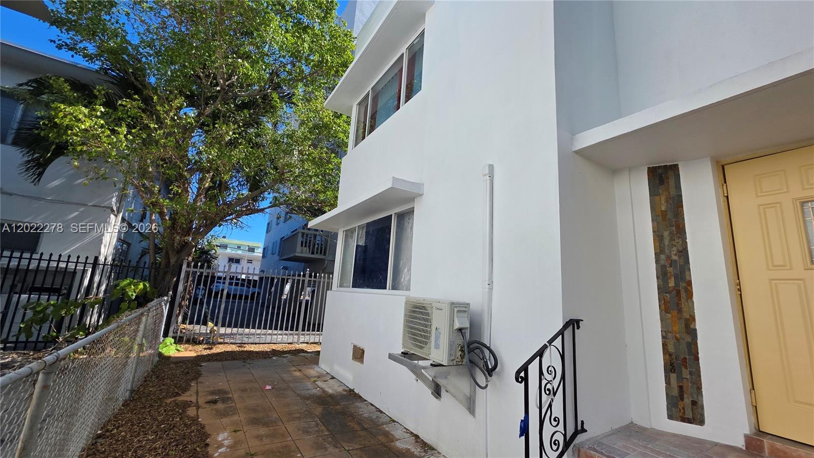 A white two-story building exterior features palm trees, windows, and mounted air conditioning units — 7629 Dickens Ave # 8, Miami Beach FL 33141, MIAMI BEACH, FL