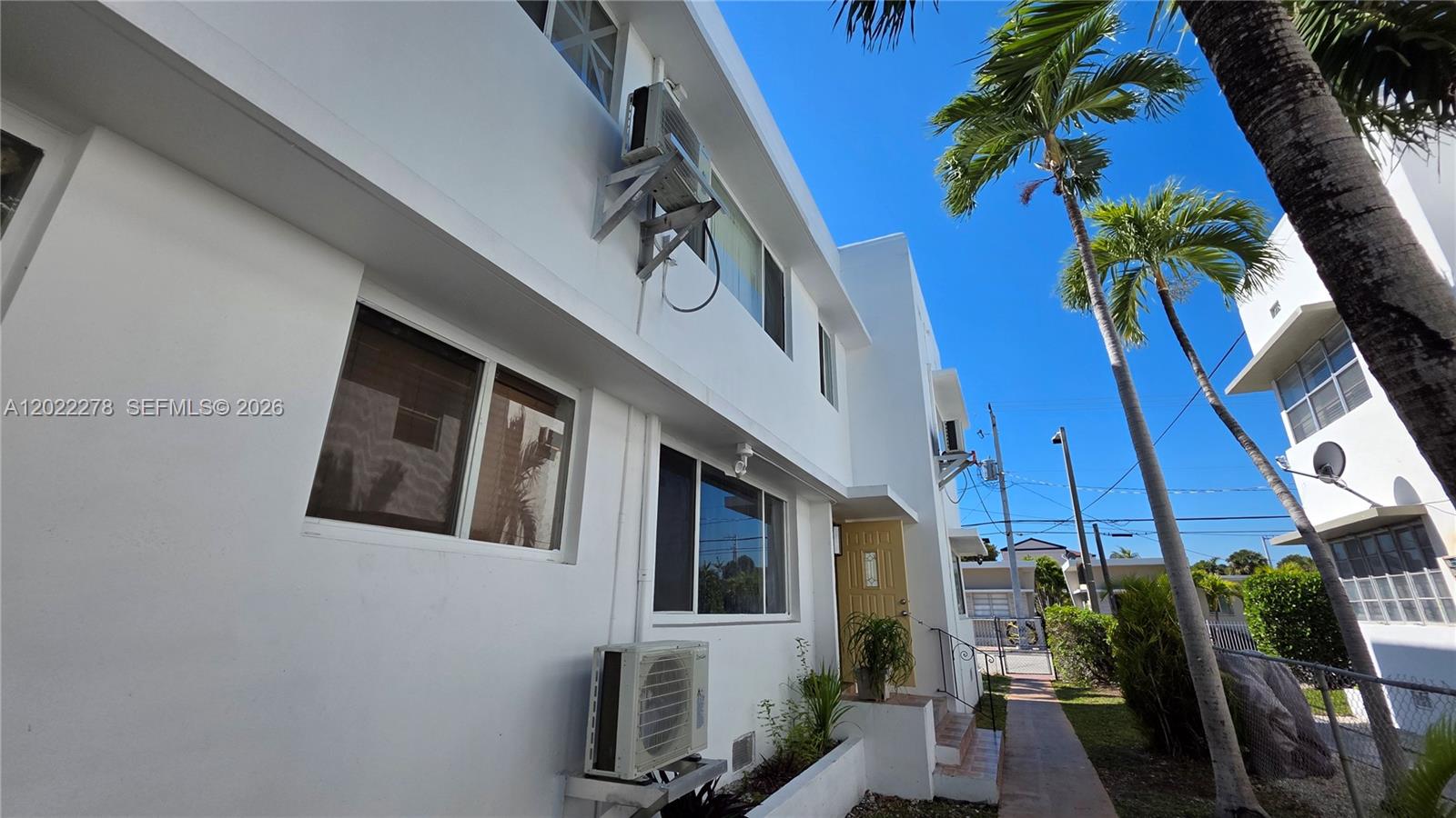 The exterior of a white two-story building features a yellow door and a wall-mounted AC unit — 7629 Dickens Ave # 8, Miami Beach FL 33141, MIAMI BEACH, FL