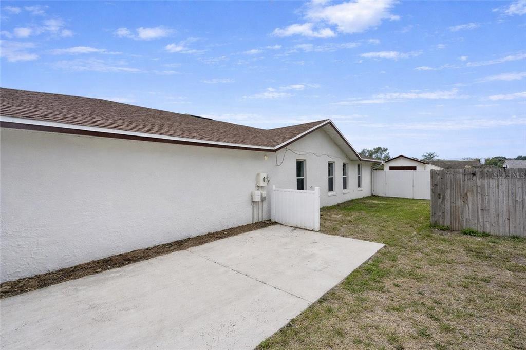 A concrete patio sits beside the white exterior wall of a house with a fenced yard — 8276 SHORT WAY, LAKELAND, FL