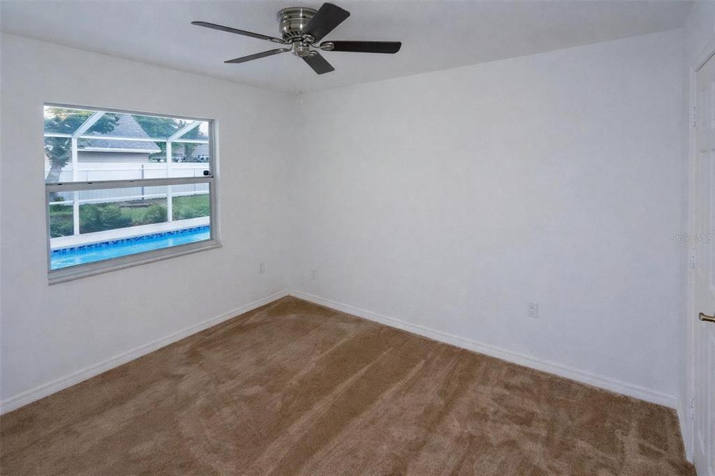 An empty bedroom with tan carpet, white walls, a ceiling fan, and a pool view — 8276 SHORT WAY, LAKELAND, FL
