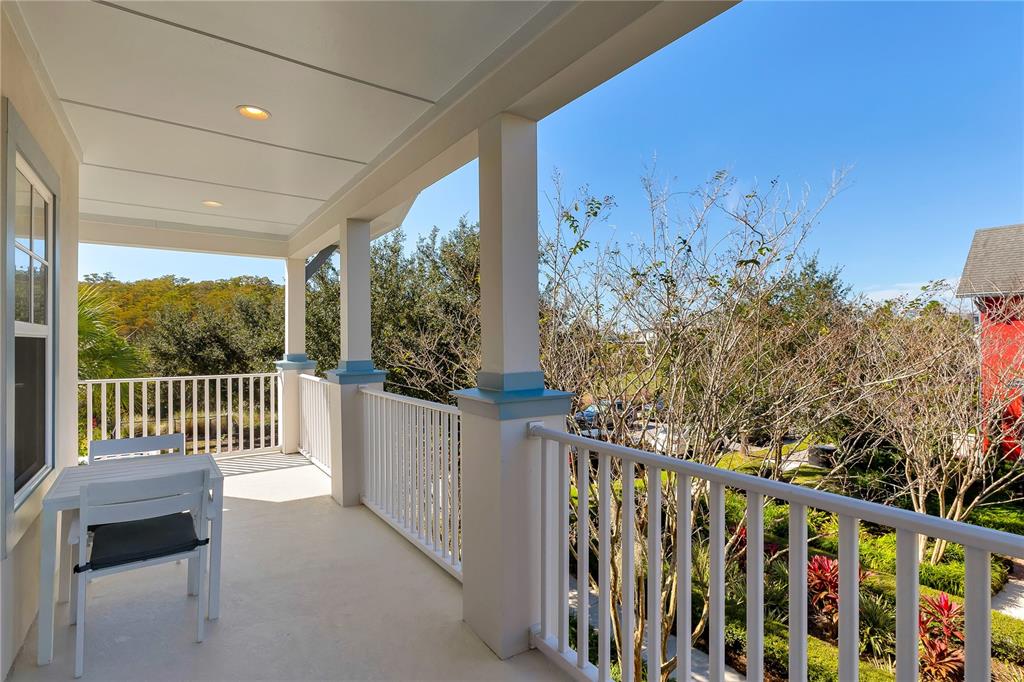 A covered balcony features white railings, a small table with chairs, and views of trees — 14080 AGRE LANE, ORLANDO, FL
