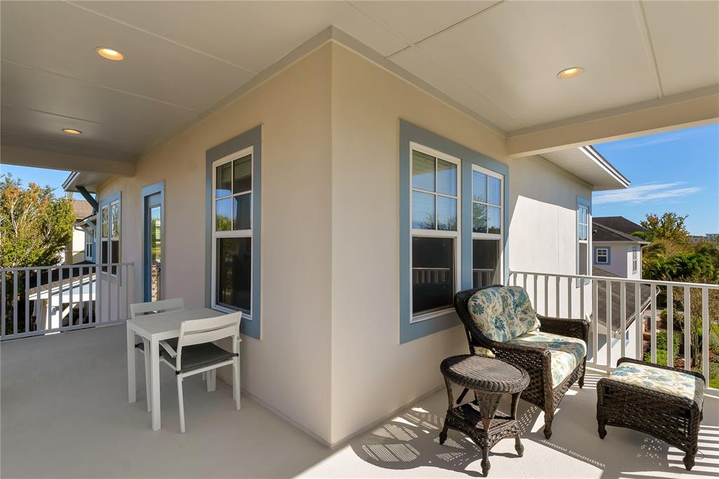 A covered balcony features a small dining set, wicker lounge furniture, and light-colored exterior walls — 14080 AGRE LANE, ORLANDO, FL