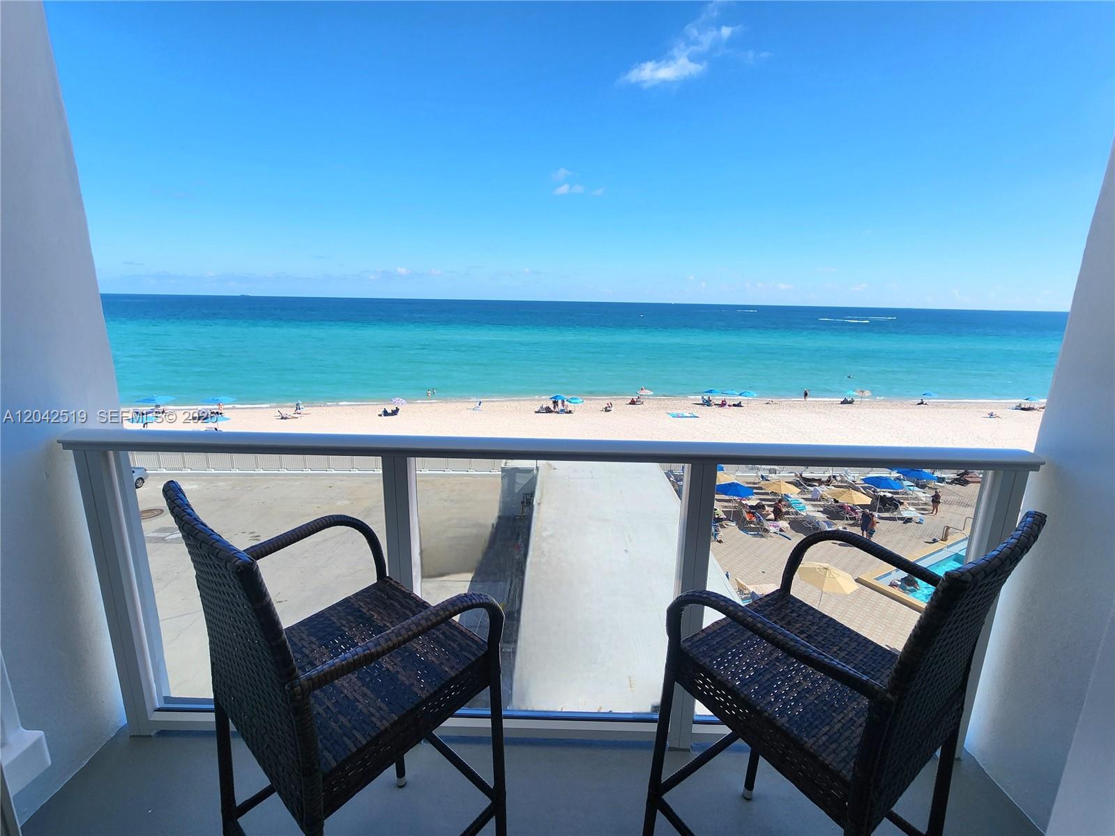 A balcony with two wicker chairs overlooks a sandy beach and the ocean — 3505 S Ocean Dr # 412, Hollywood FL 33019, HOLLYWOOD, FL