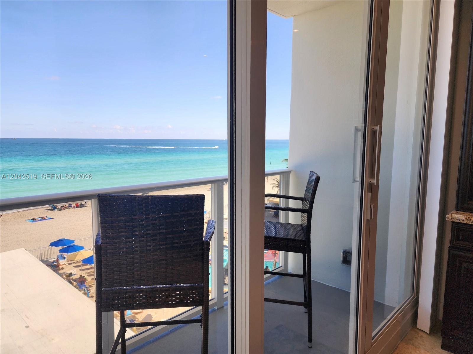 A balcony with two wicker chairs overlooks a sandy beach and the ocean — 3505 S Ocean Dr # 412, Hollywood FL 33019, HOLLYWOOD, FL