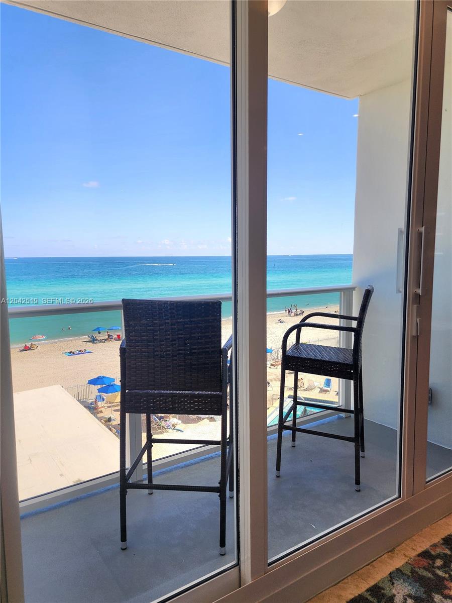 A balcony with two wicker chairs overlooks a sandy beach and the ocean — 3505 S Ocean Dr # 412, Hollywood FL 33019, HOLLYWOOD, FL