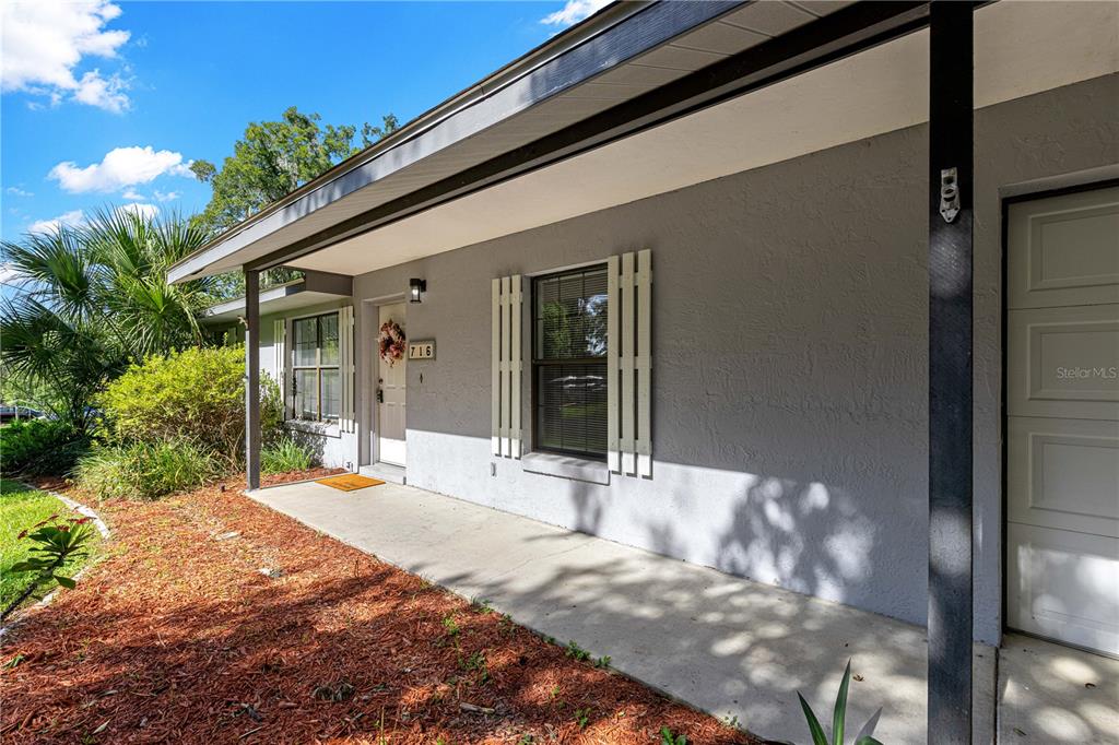 A gray house exterior features a covered concrete porch, white shutters, and a front door — 716 SE 31ST AVENUE, OCALA, FL