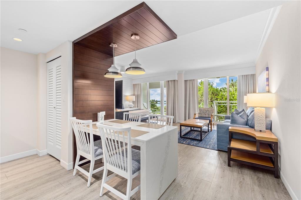 A dining area with a white marble table and two chairs sits before a living room — 240 SANDS POINT ROAD UNIT 4102, LONGBOAT KEY, FL