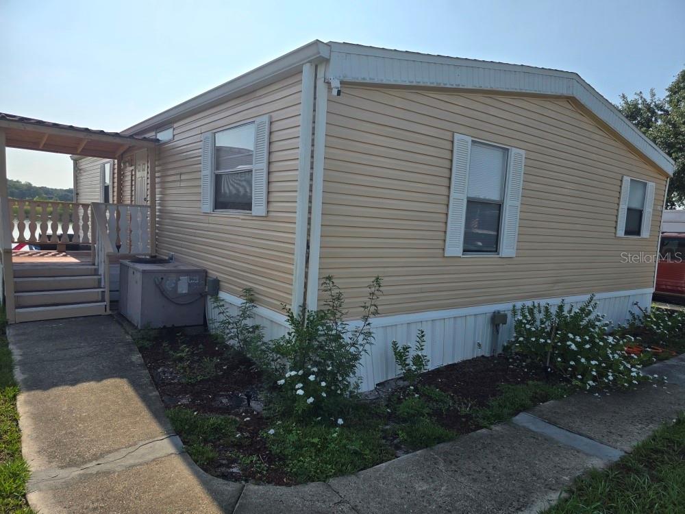 A tan mobile home with a covered porch, concrete walkway, and small landscaping beds — 1125 PENINSULAR DRIVE, LAKE WALES, FL