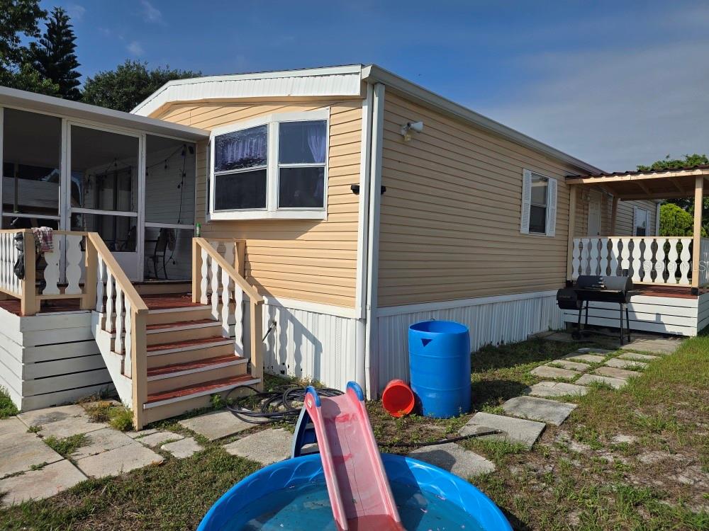 A tan mobile home features a screened porch, a wooden deck, and a small pool — 1125 PENINSULAR DRIVE, LAKE WALES, FL