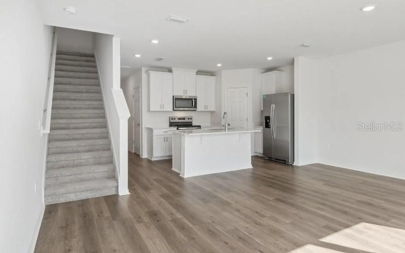 An open-concept kitchen with white cabinetry and stainless steel appliances sits beside a carpeted staircase — 16257 BIRD OF PARADISE AVENUE, CLERMONT, FL