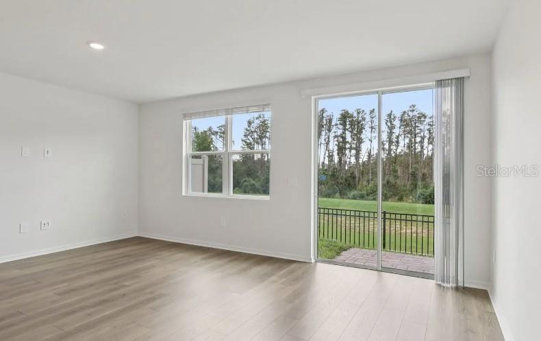 An empty room with light wood-look flooring, a window, and a sliding glass door — 16257 BIRD OF PARADISE AVENUE, CLERMONT, FL
