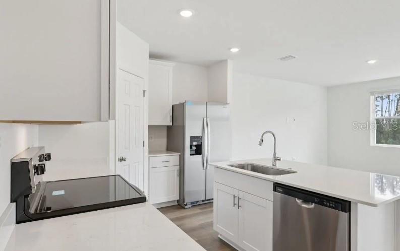 A modern kitchen features white cabinets, stainless steel appliances, and a quartz-topped island with sink — 16257 BIRD OF PARADISE AVENUE, CLERMONT, FL