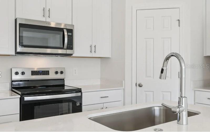 A kitchen features white cabinets, stainless steel appliances, a quartz countertop, and a sink island — 16257 BIRD OF PARADISE AVENUE, CLERMONT, FL