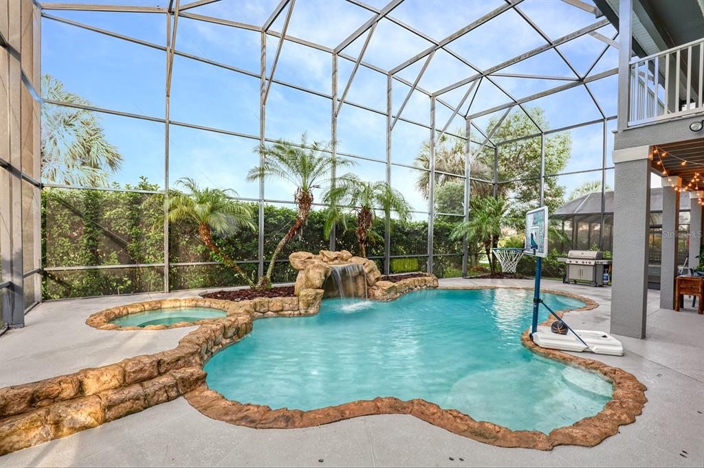 A screened-in pool area features a rock waterfall, a hot tub, and a basketball hoop — 13412 FOX GLOVE STREET, WINTER GARDEN, FL