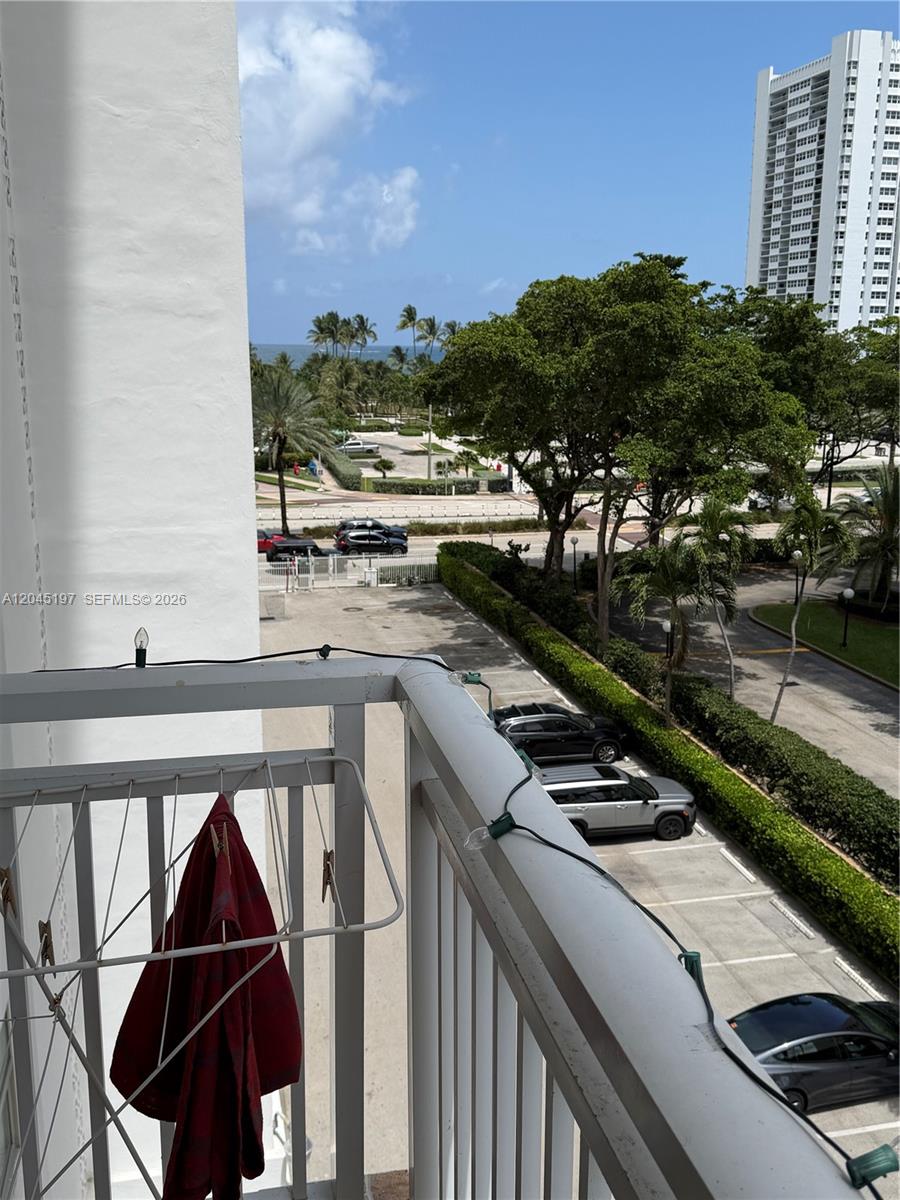 A balcony view overlooks a parking lot, trees, and the ocean in the distance — 1849 S Ocean Dr # 508, Hallandale Beach FL 33009, HALLANDALE BEACH, FL