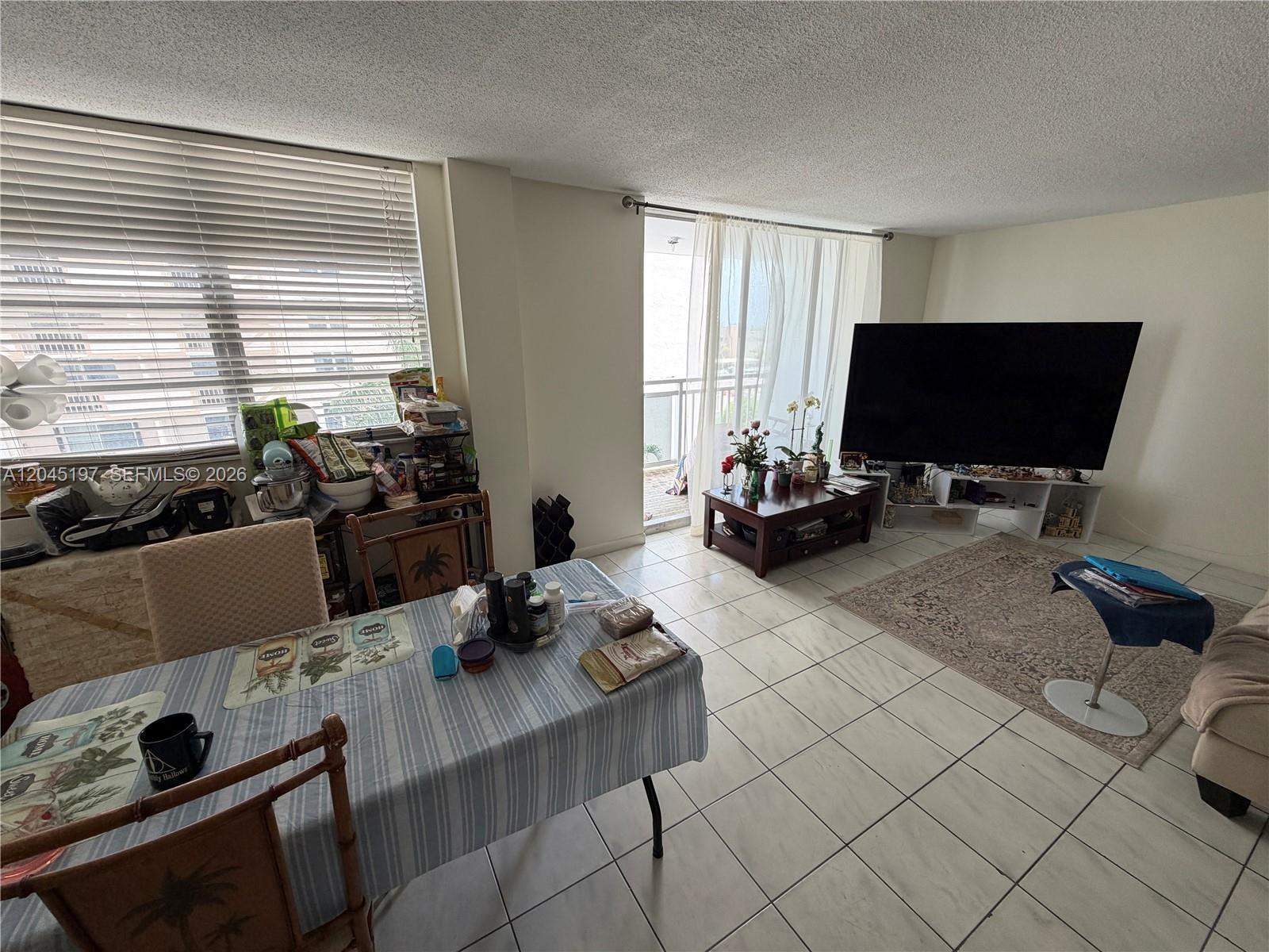 This living and dining area features tile flooring, a large television, and a balcony entrance — 1849 S Ocean Dr # 508, Hallandale Beach FL 33009, HALLANDALE BEACH, FL