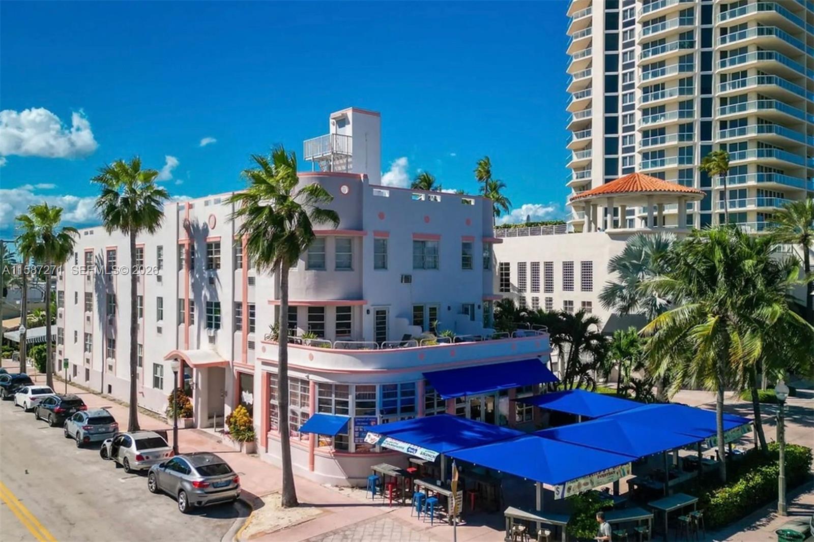 An exterior view of a multi-story Art Deco building with a blue-canopied outdoor restaurant area — 7300 Ocean Ter, Miami Beach FL 33141, MIAMI BEACH, FL