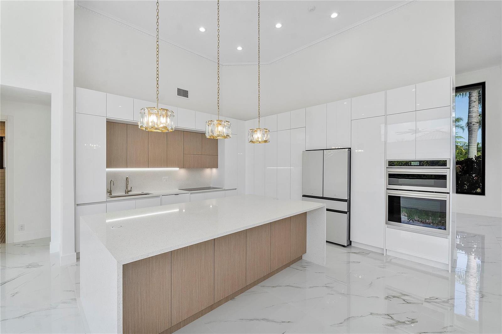 A modern kitchen features white glossy cabinets, wood accents, a quartz island, and marble flooring — 410 Sabal Way, Weston FL 33326, WESTON, FL