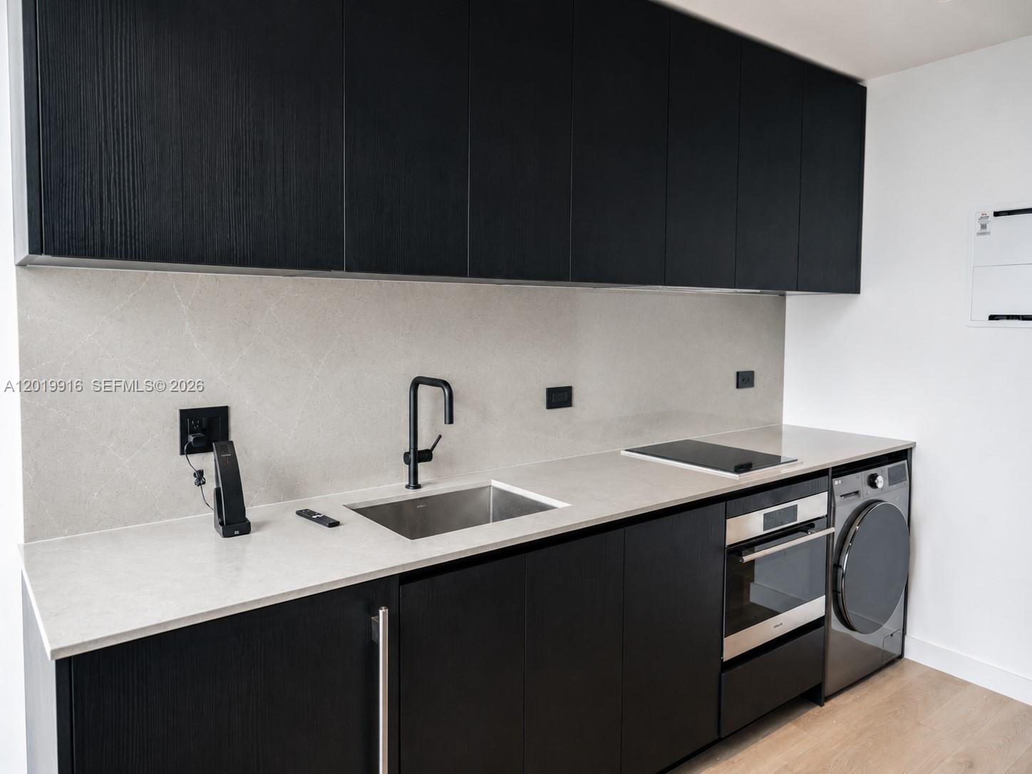 A modern kitchen features black cabinetry, a light stone countertop, and an integrated laundry machine — 20 NE 11 St # 3112B, Miami FL 33132, MIAMI, FL