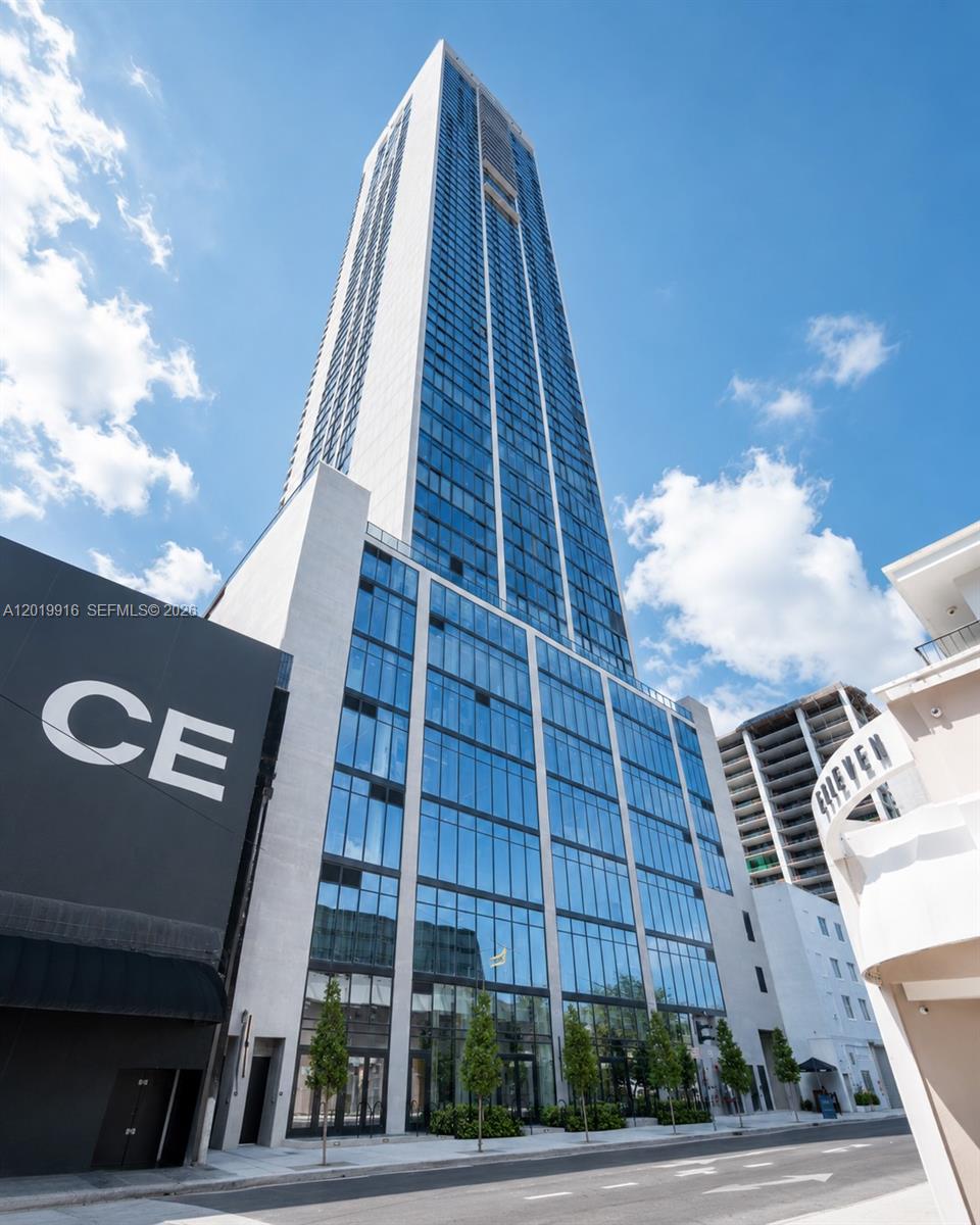 A low-angle view of a modern glass skyscraper with a white facade against a blue sky — 20 NE 11 St # 3112B, Miami FL 33132, MIAMI, FL