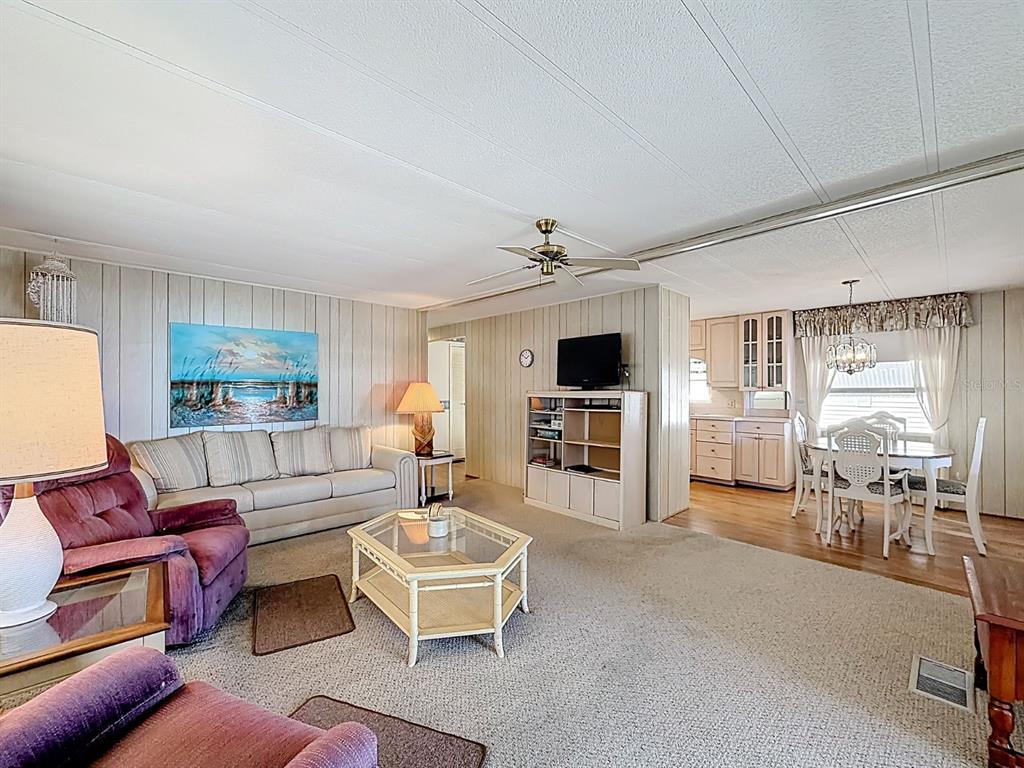 A living room with beige carpet, wood-paneled walls, a ceiling fan, and an adjacent dining area — 1100 BELCHER ROAD S UNIT 561, LARGO, FL