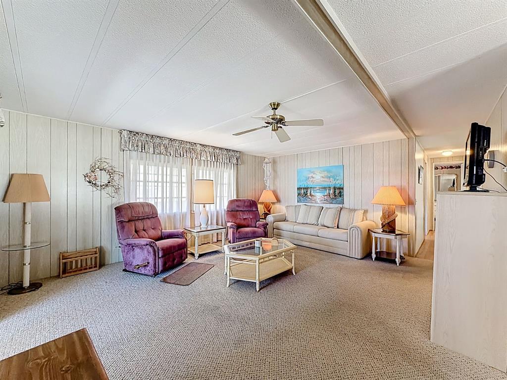 A living room features beige carpet, wood-paneled walls, two purple recliners, and a beige sofa — 1100 BELCHER ROAD S UNIT 561, LARGO, FL