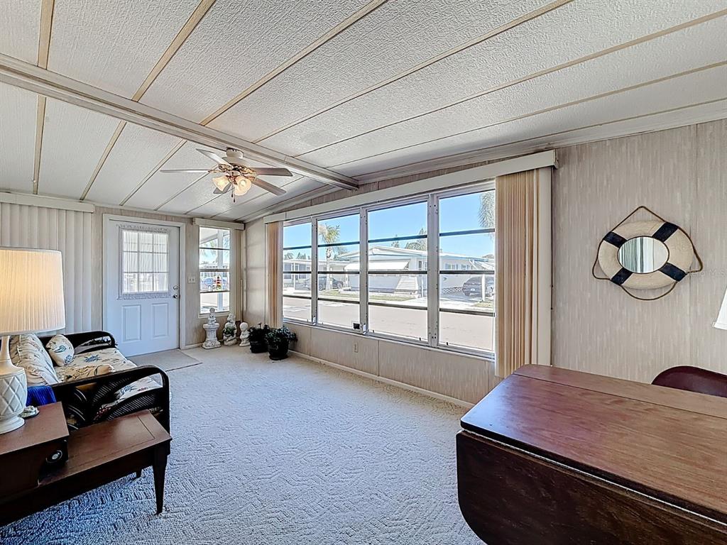 A sunroom features a ceiling fan, large windows, carpeted flooring, and a wooden dining table — 1100 BELCHER ROAD S UNIT 561, LARGO, FL