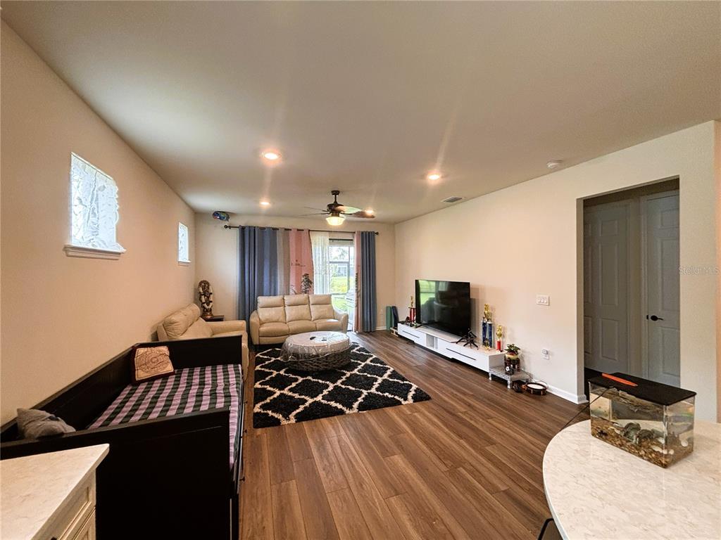 A living room features wood-look flooring, a black and white rug, and a television console — 12444 GOLDEN SAGE DRIVE, SARASOTA, FL