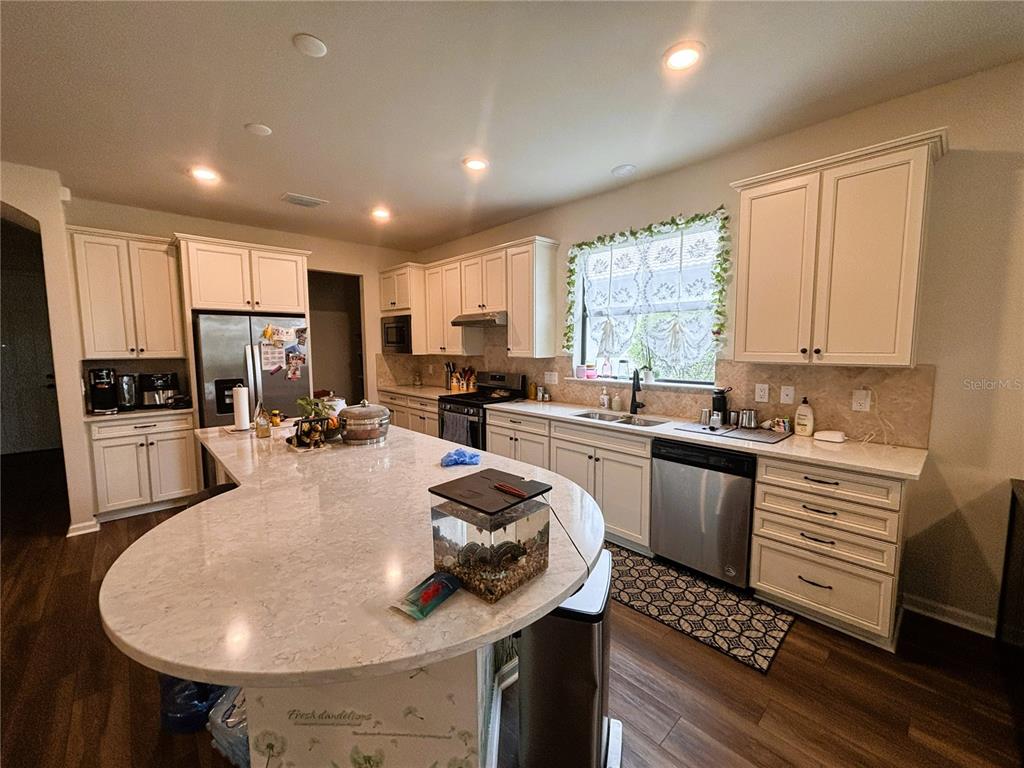 A kitchen features white cabinets, a large curved island with a countertop, and stainless appliances — 12444 GOLDEN SAGE DRIVE, SARASOTA, FL