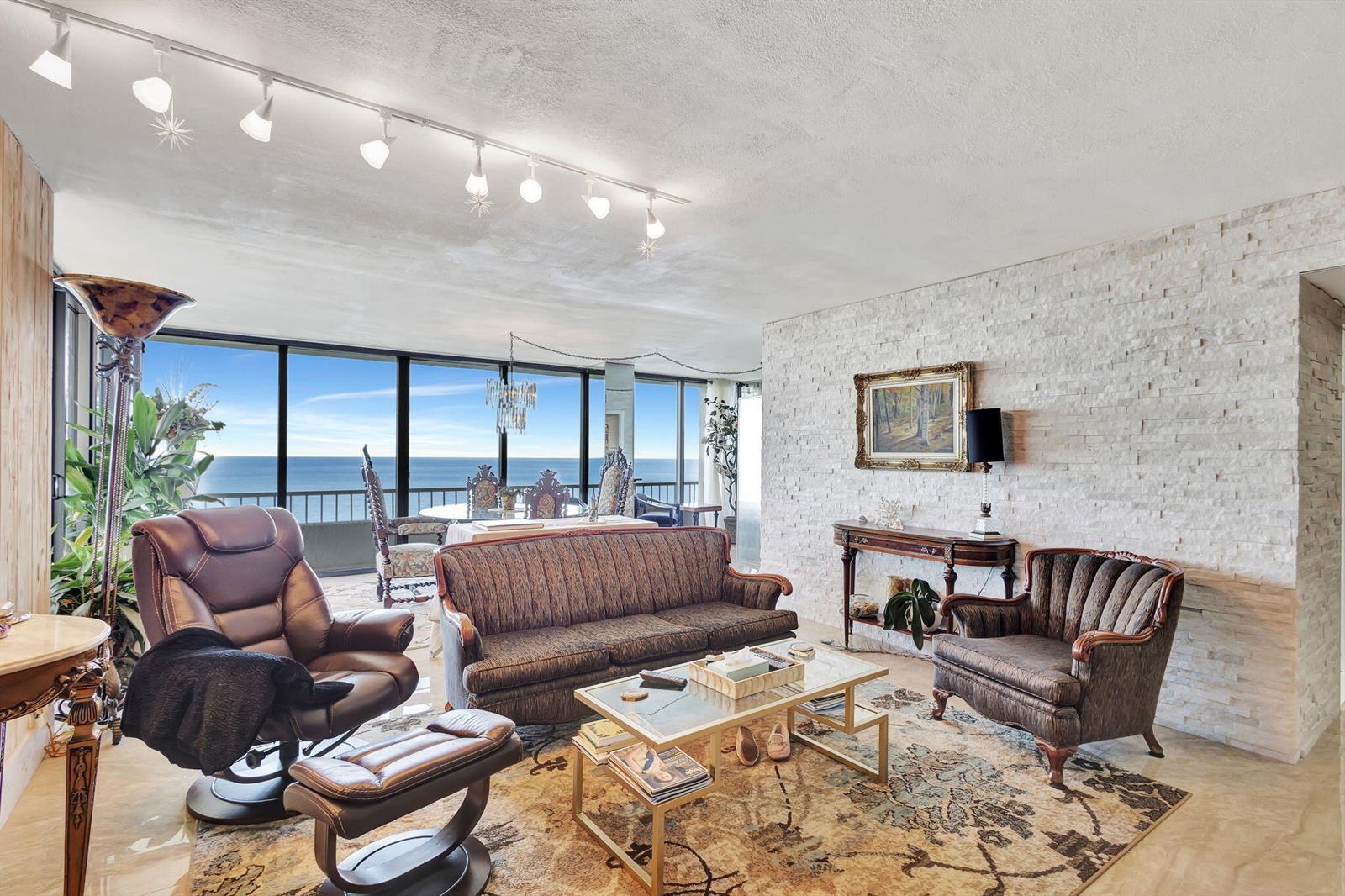 A living room with a stone accent wall, track lighting, and floor-to-ceiling ocean views — 5550 N Ocean Drive # 21c, Singer Island FL 33404, SINGER ISLAND, FL