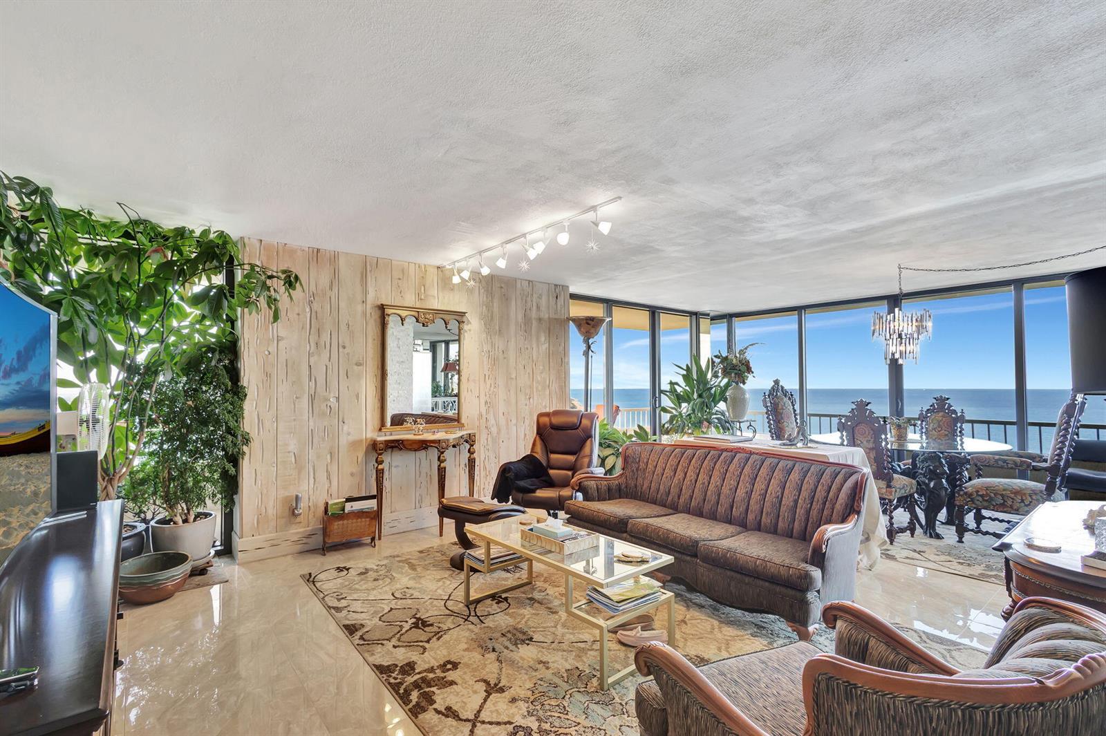 A living room with a striped sofa, glass coffee table, and floor-to-ceiling ocean views — 5550 N Ocean Drive # 21c, Singer Island FL 33404, SINGER ISLAND, FL