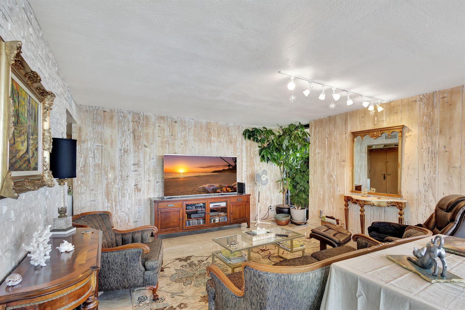 A living room features wood-paneled walls, a television on a wooden console, and patterned furniture — 5550 N Ocean Drive # 21c, Singer Island FL 33404, SINGER ISLAND, FL