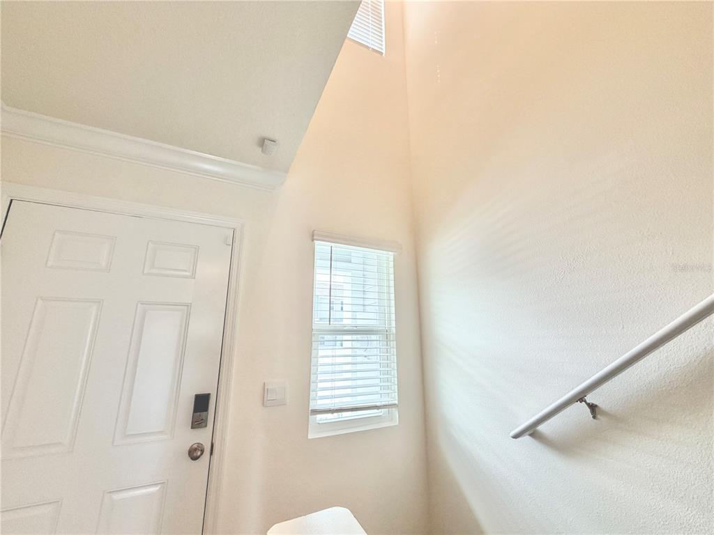 A high-ceilinged entryway features a white door, a window with blinds, and a handrail — 8229 SW 67TH AVENUE, OCALA, FL
