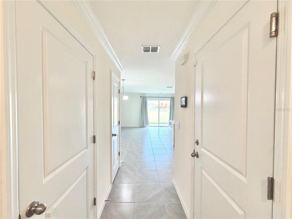 A hallway with white doors leads to an open living area with tile flooring — 8229 SW 67TH AVENUE, OCALA, FL