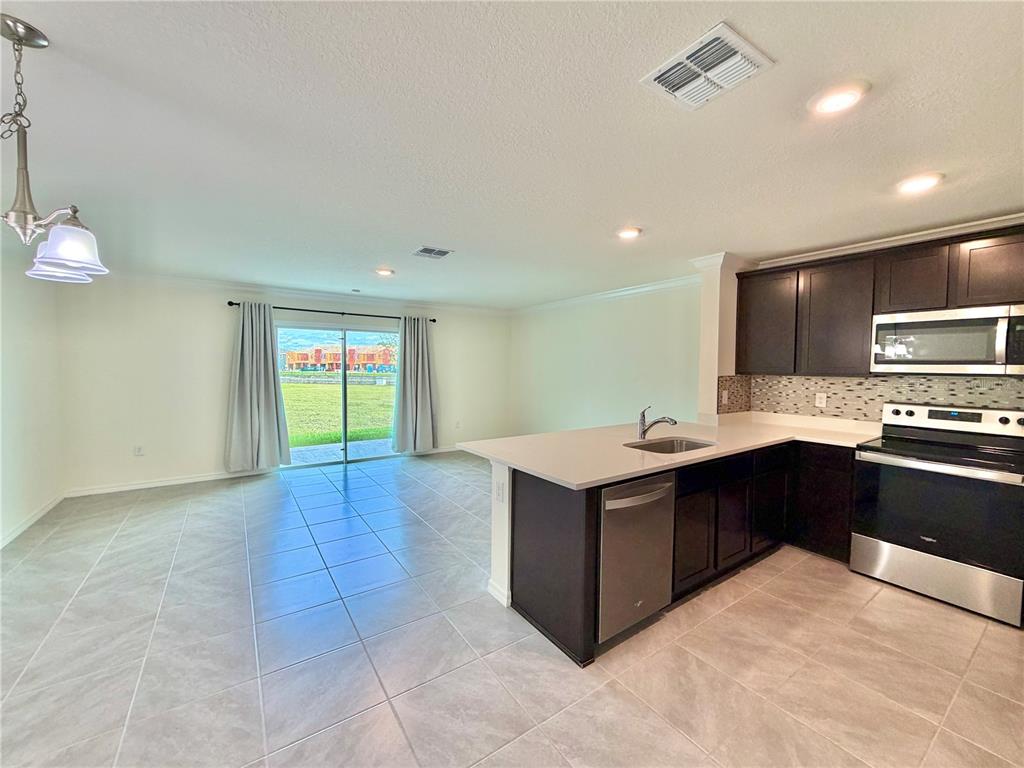 A kitchen with dark cabinets and stainless steel appliances opens to a tiled living area — 8229 SW 67TH AVENUE, OCALA, FL