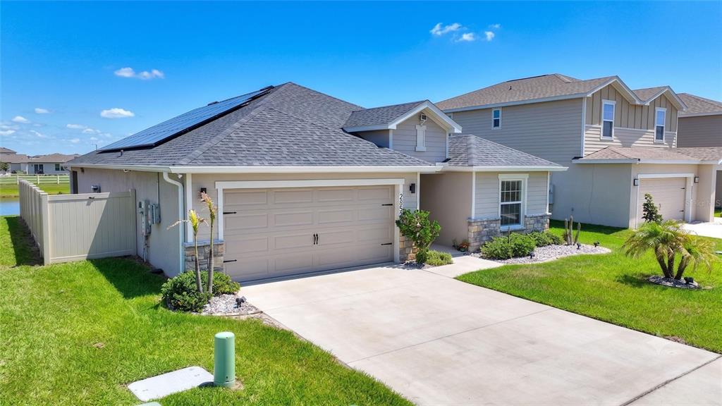 A single-story house with a tan garage, stone accents, and solar panels on the roof — 2852 SAN MARCO WAY, WINTER HAVEN, FL