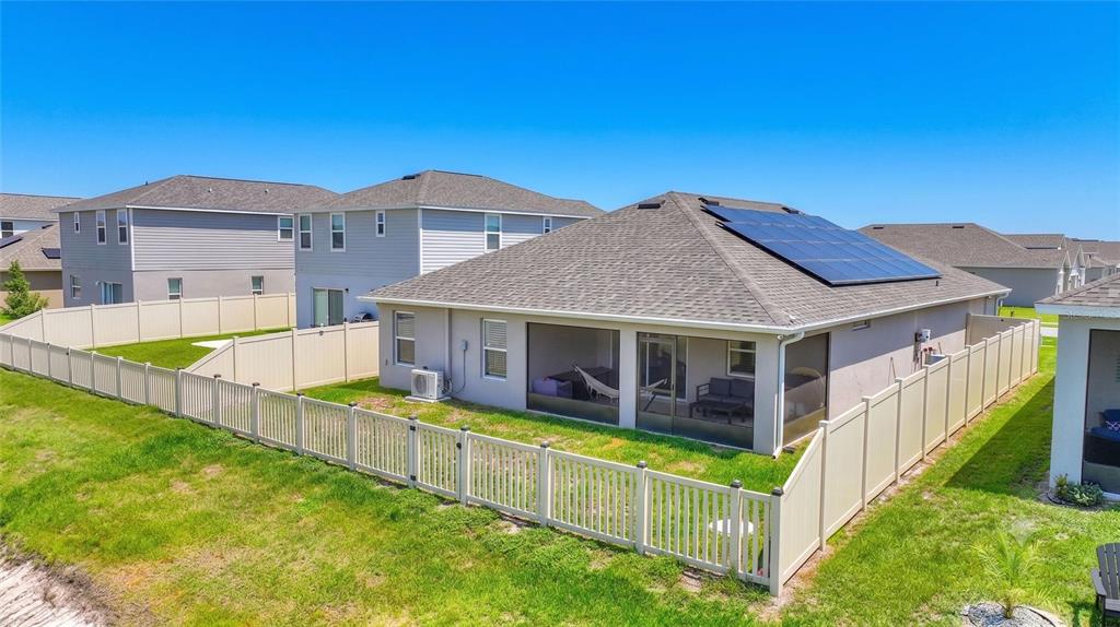 A backyard view of a house with a screened-in patio and roof-mounted solar panels — 2852 SAN MARCO WAY, WINTER HAVEN, FL