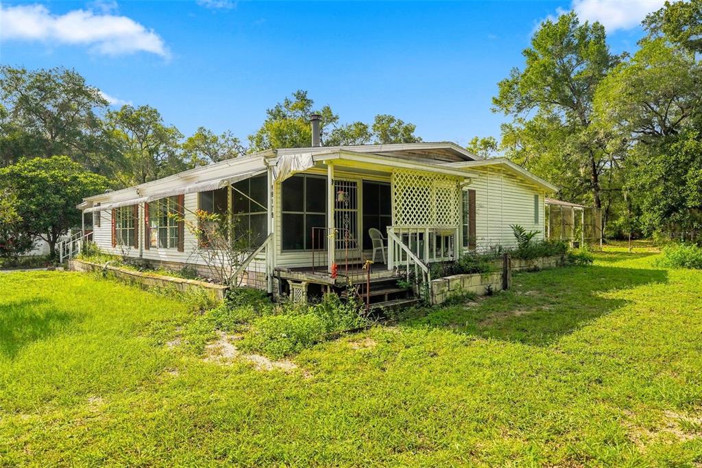 A single-story mobile home with a screened-in porch and lattice detailing sits on a lawn — 16179 WISCON ROAD, BROOKSVILLE, FL