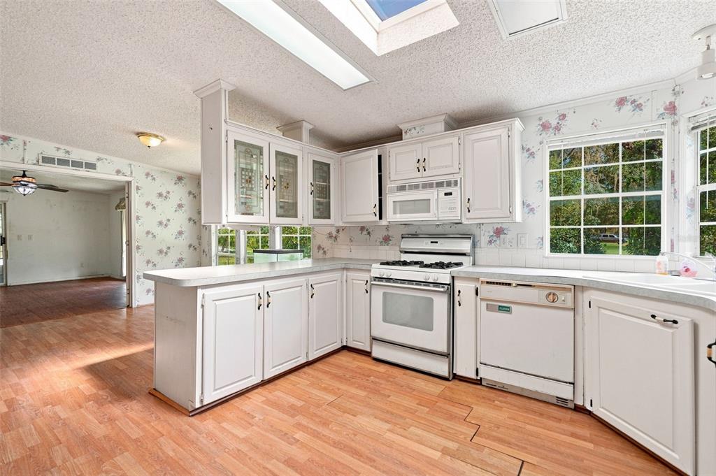 A kitchen with white cabinets, laminate countertops, a gas range, and floral wallpaper — 16179 WISCON ROAD, BROOKSVILLE, FL