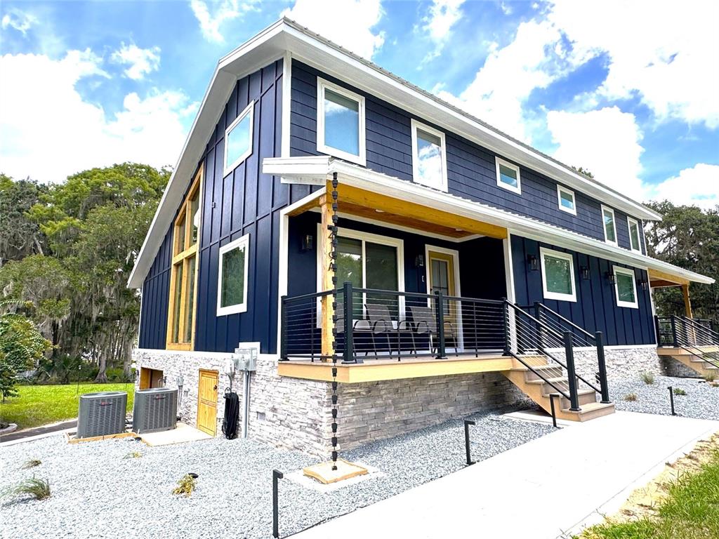 A two-story house with dark blue vertical siding, stone foundation, and a front porch — 419 N APOPKA AVENUE, INVERNESS, FL